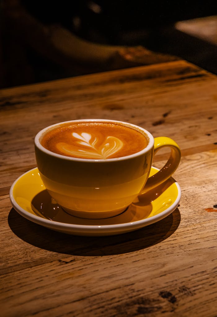 Cozy cappuccino with latte art in a yellow cup, set on a rustic wooden table.